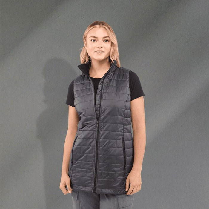 Women's Telluride Lightweight Packable Insulated Puffer Vest - A woman is wearing a lightweight, packable insulated puffer vest in dark grey, featuring a zip front and a high collar.