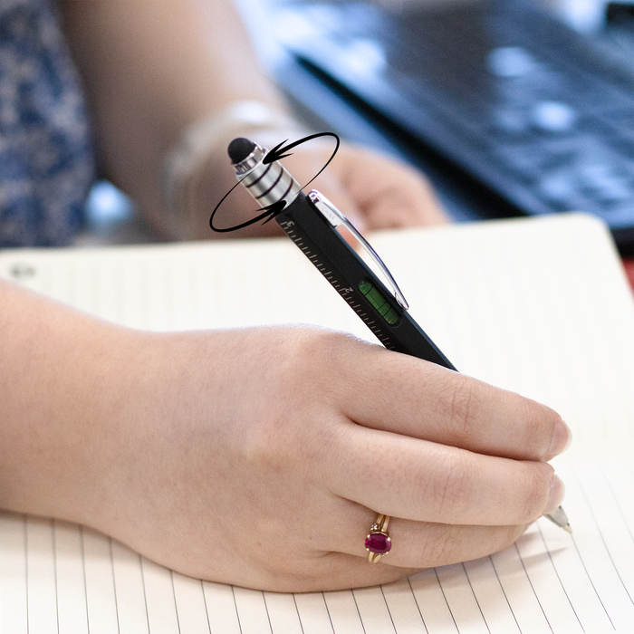 The Balance Pen - A black and silver pen with a unique balance design is held above a notebook with blank pages.