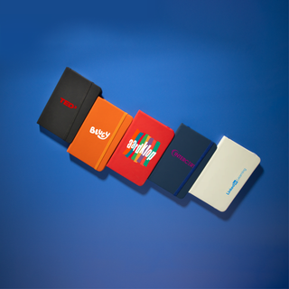 Minichroma A6 Notebook - A collection of five Minichroma A6 Notebooks in various colours: red, orange, blue, navy, and white, each featuring a logo.