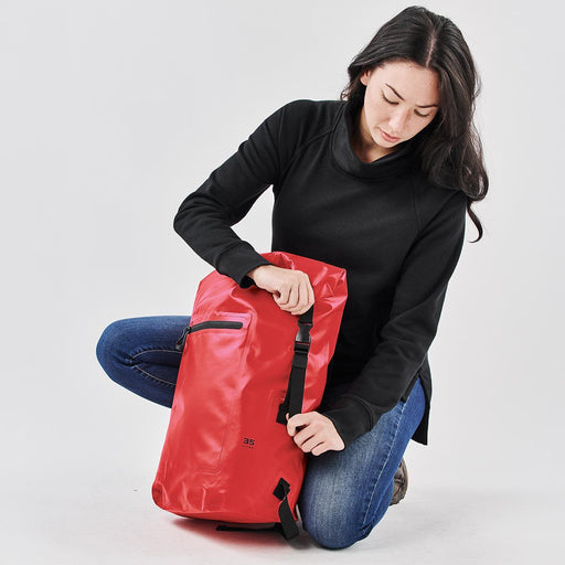 Cirrus Backpack 35 - A red backpack with a sleek design, featuring a zippered pocket and adjustable straps, held by a person in black attire.